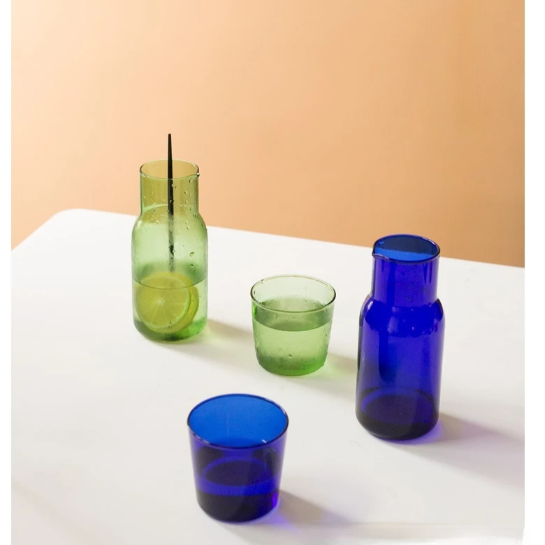 Set of green and blue glass tumblers on a white surface with a beige background