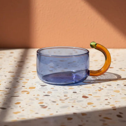 Clear glass mug with a unique handle on a terrazzo table with a warm-toned wall background
