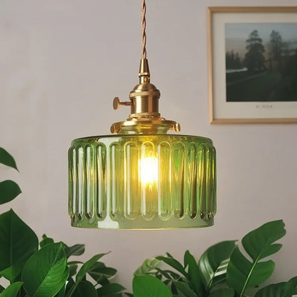 Green ribbed pendant light with gold fixture on a neutral wall with a plant and framed picture in the background.