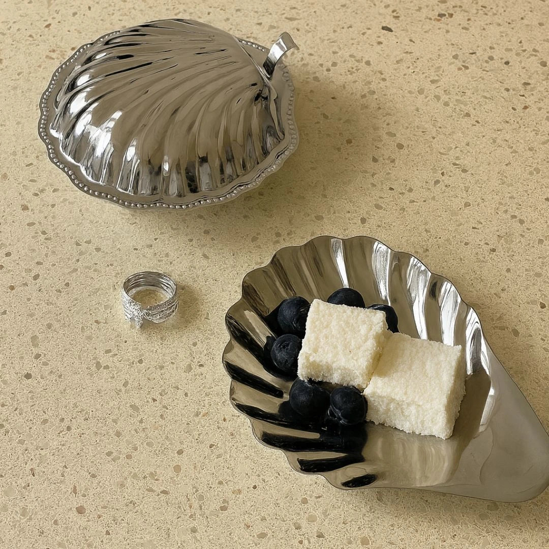 Silver leaf-shaped dish with cheese and blueberries on a beige surface
