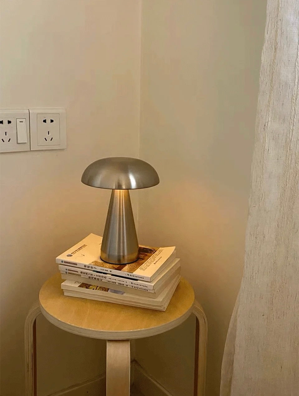 Small round wooden table with a metallic lamp on top against a neutral wall.