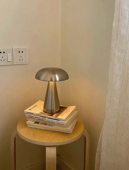 Small round wooden table with a metallic lamp on top against a neutral wall.