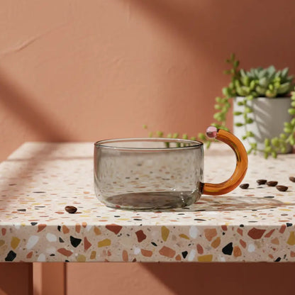 A glass teacup on a terazzo tabletop with a plant behind.