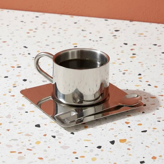 Silver cup and saucer set on a terrazzo-patterned surface