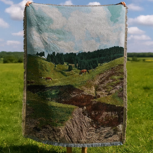 Blanket with a landscape of horses in a field held up against a grassy background