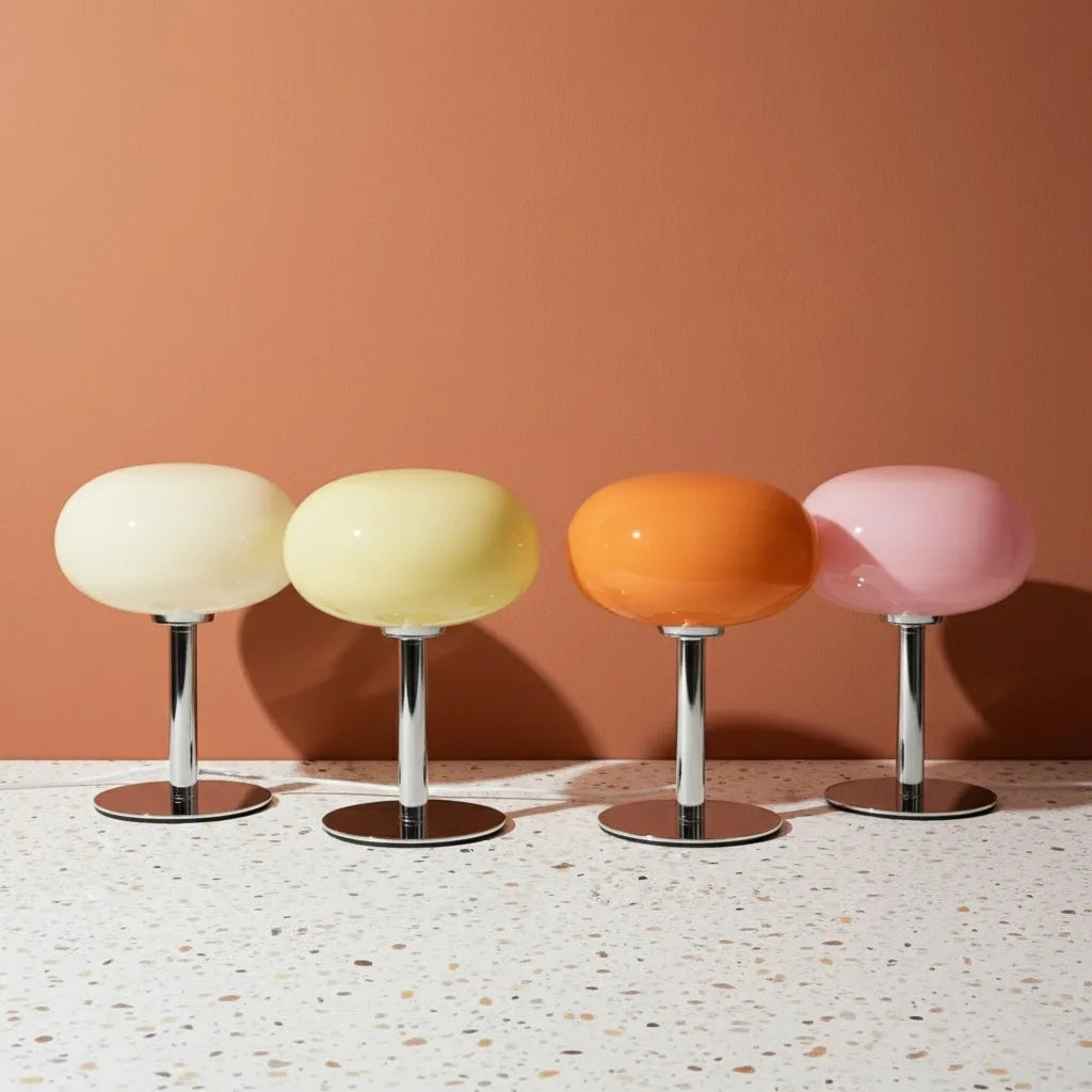 Four colorful stools with round seats and metallic bases on a terrazzo floor against a peach wall.