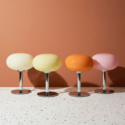 Four colorful stools with round seats and metallic bases on a terrazzo floor against a peach wall.