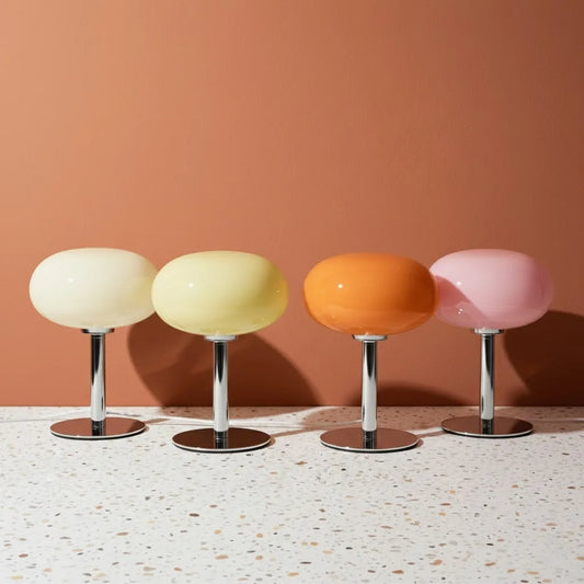 Four colorful stools with round seats and metallic bases on a terrazzo floor against a peach wall.