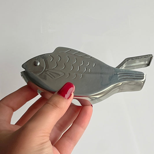 Metallic fish-shaped object held by a hand with red nail polish on a white background