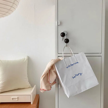 White shopping bag with 'Victoria Bakery' text hanging on a door handle next to a pillow and small wooden table.