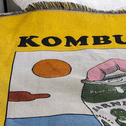 Textile with 'KOMBU' and images of a bun, hand, and can on a yellow background