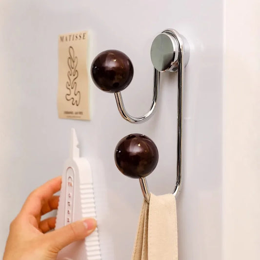 Metallic wall hook with wooden knobs holding a tube of toothpaste and a towel on a white wall.