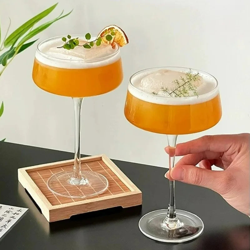 Two cocktails with orange liquid and white foam, one being held by a hand on a dark surface.