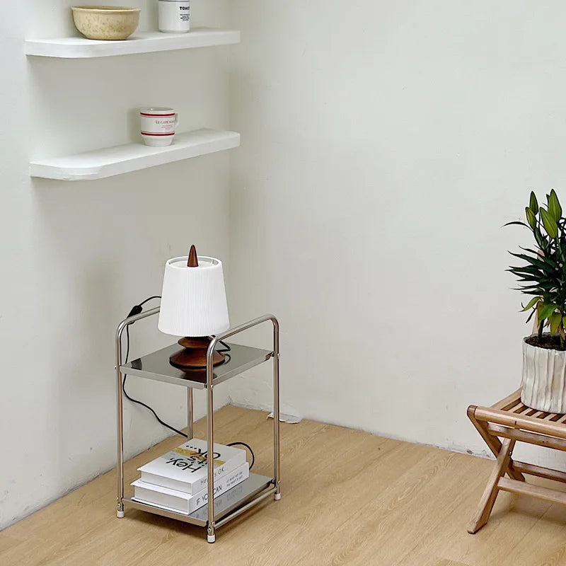 A metal storage cart with a lamp on it undernearth shelving 