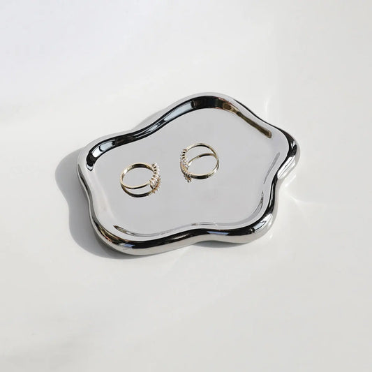 Silver jewelry tray with two gold rings on a white background