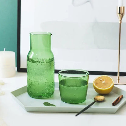 Green glass carafe and cup on a white tray with lemon and cinnamon.