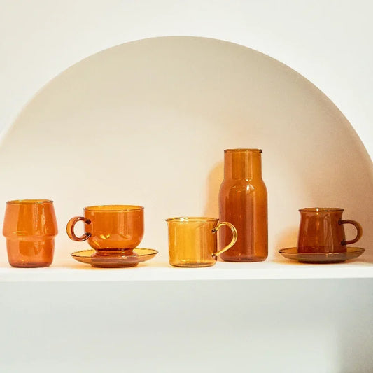 Set of orange ceramic cups and a carafe on a white surface with a neutral background