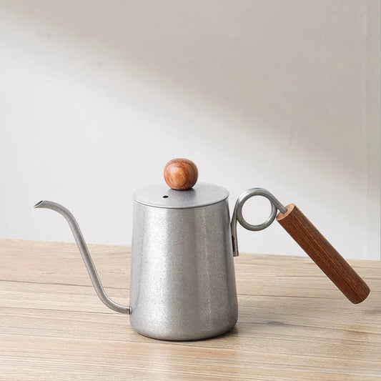 Silver kettle with wooden handle and spout on a light wooden surface