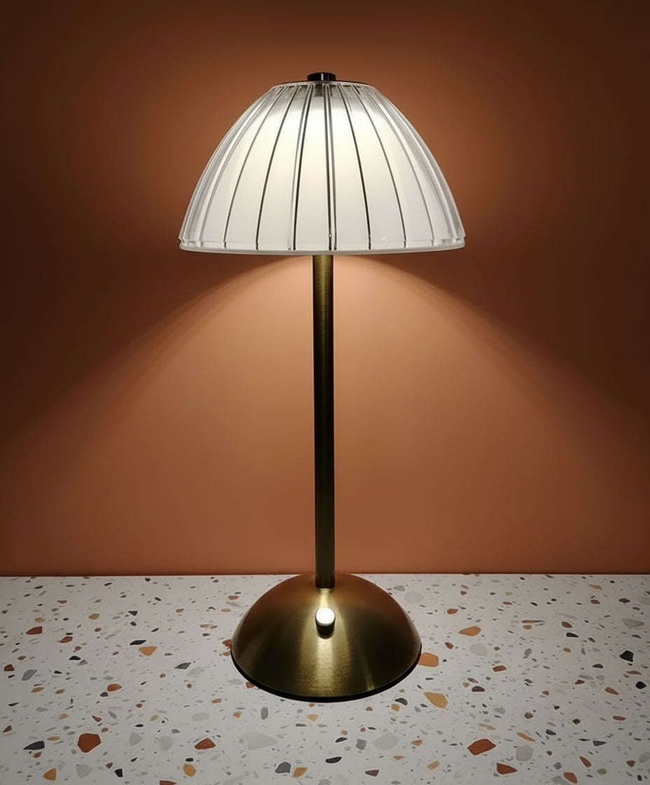 A glass lamp with gold stem omitting white light. Terazzo tabletop and teracotta coloured wall.