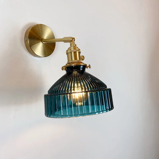 Wall-mounted lamp with blue glass shade and brass fixture on a white wall.