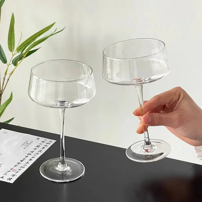 Two clear glass wine glasses on a black surface with a white background