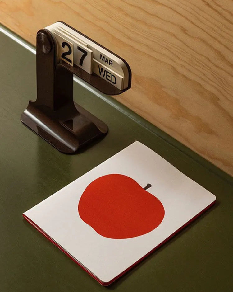 Small calendar on a surface with a red apple illustration on a card below.