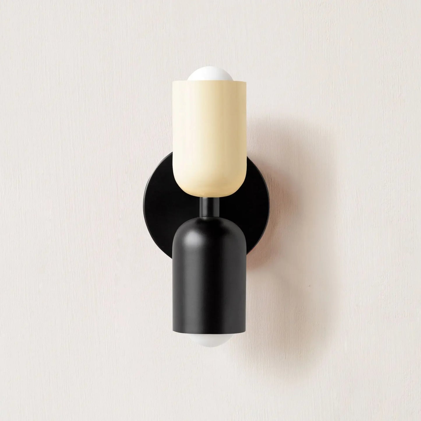 Wall-mounted light fixture with black base and beige shade on a white background
