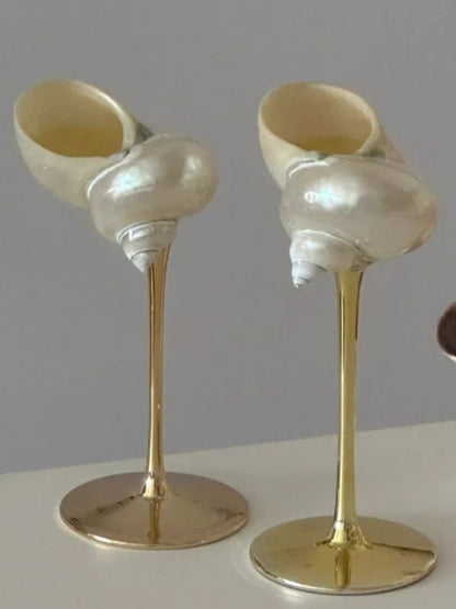 Two decorative items resembling seashells on gold stands against a gray background