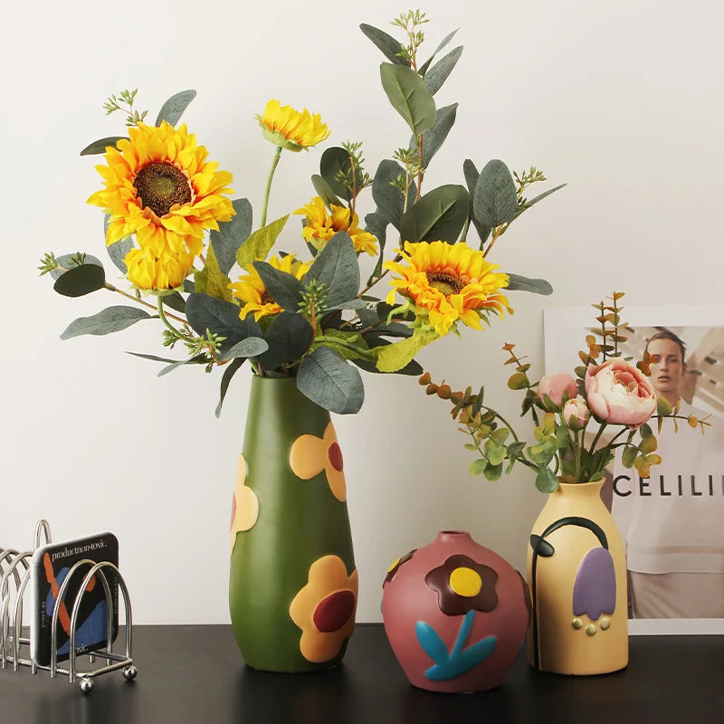 Three colorful vases with floral designs on a table against a white wall.