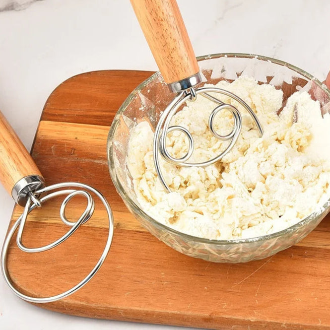 Flour mixer being used to mix flour in a glass bowl on a wooden cutting board.