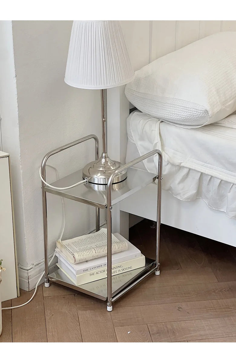 A metal trolley cart with wheels with books on the bottom shelf and a lamp on the top