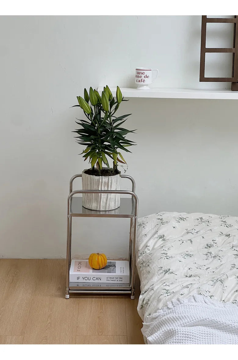A metal storage cart with a plant pot on the top shelf. Next to a floor bed. 