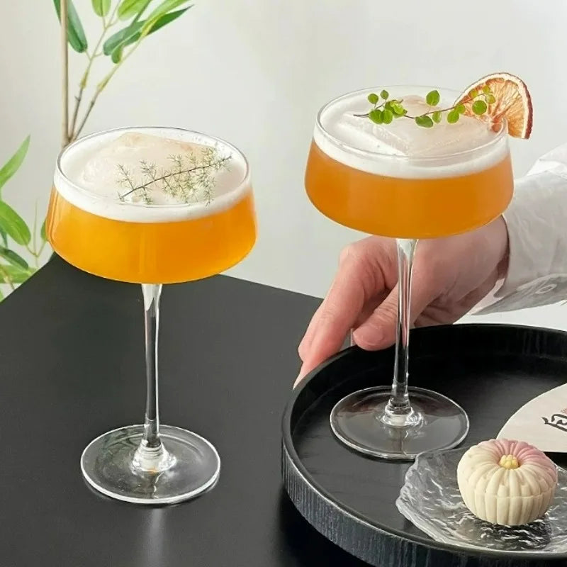 Two cocktails in glasses with a hand holding one, on a black tray with a white background.