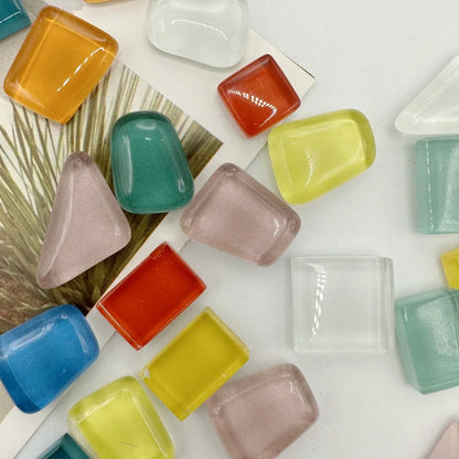 Colorful glass stones on a white surface with a plant leaf in the background