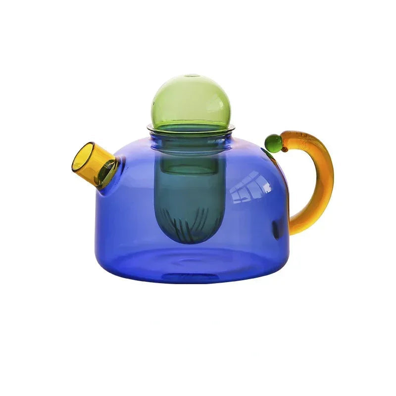 Colorful glass teapot with a blue body, green lid, and orange handle on a white background.