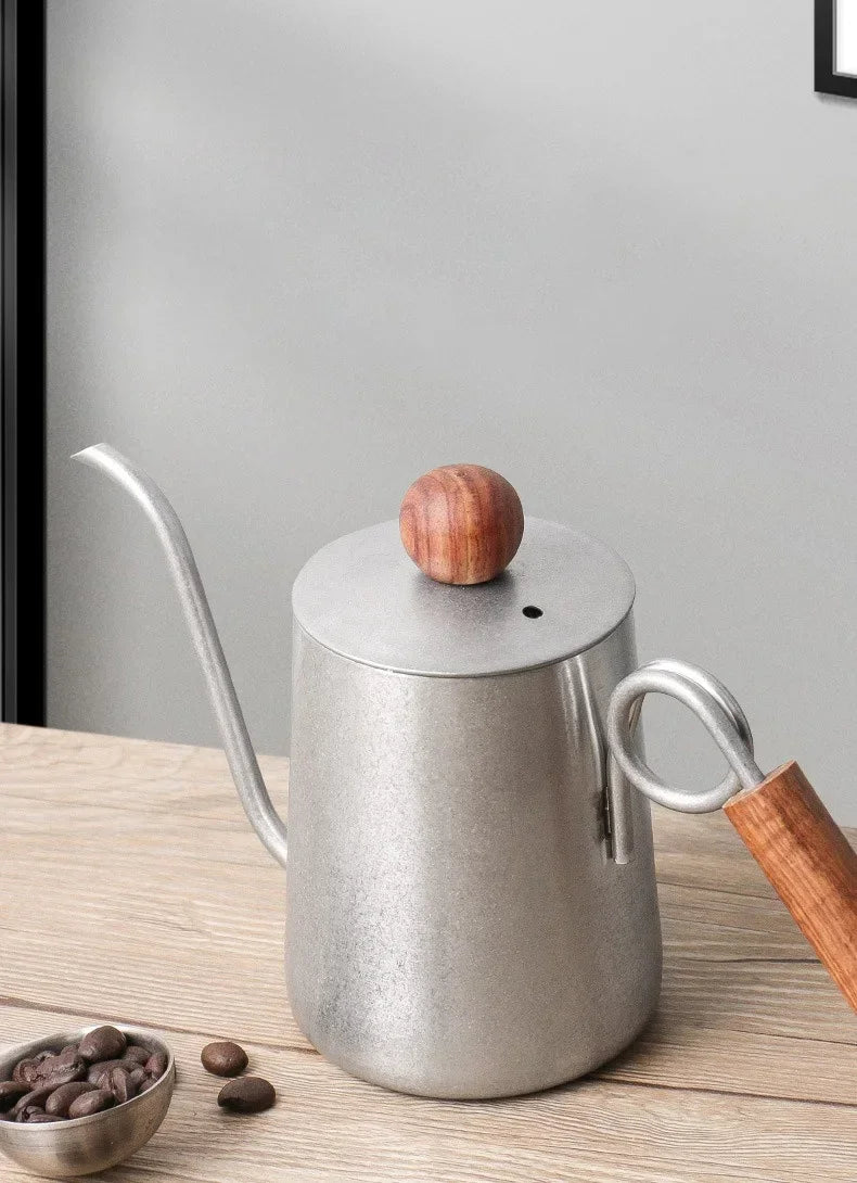 Stainless steel kettle with wooden handle and lid on a wooden surface