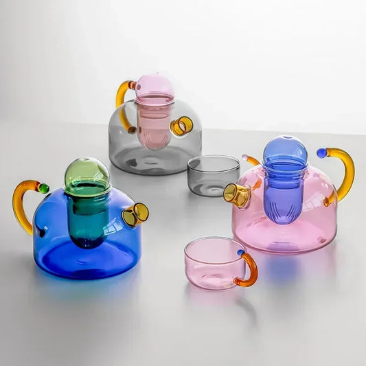 Set of colorful glass teapots and cups on a light gray background