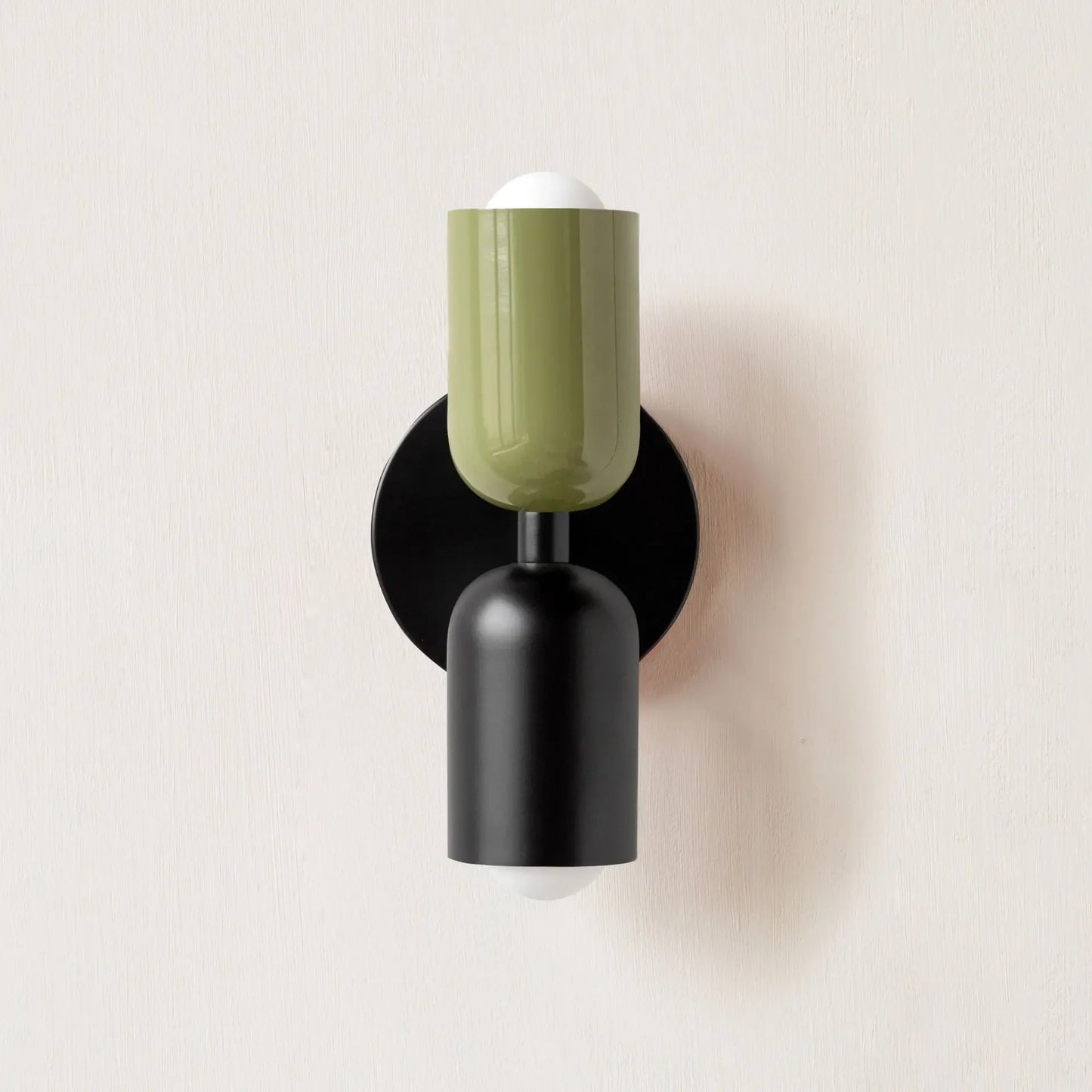 Wall-mounted lamp with green glass shade and black base on a light beige background