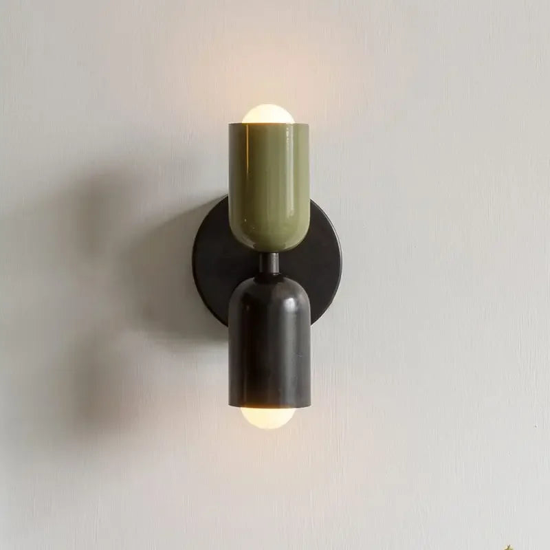 Wall-mounted light fixture with a green and black design on a plain wall.