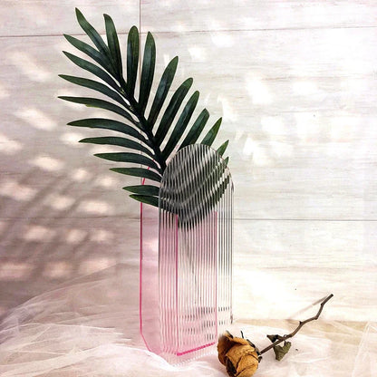 A cylindrical pink ribbed vase on white backdrop with a yellow rose next to it