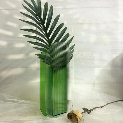 A cylindrical green ribbed vase on white backdrop with a yellow rose next to it