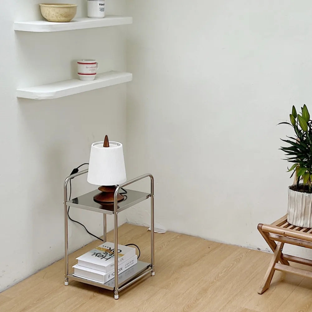 A metal trolley cart with wheels. One shelf contains books and one a lamp. 