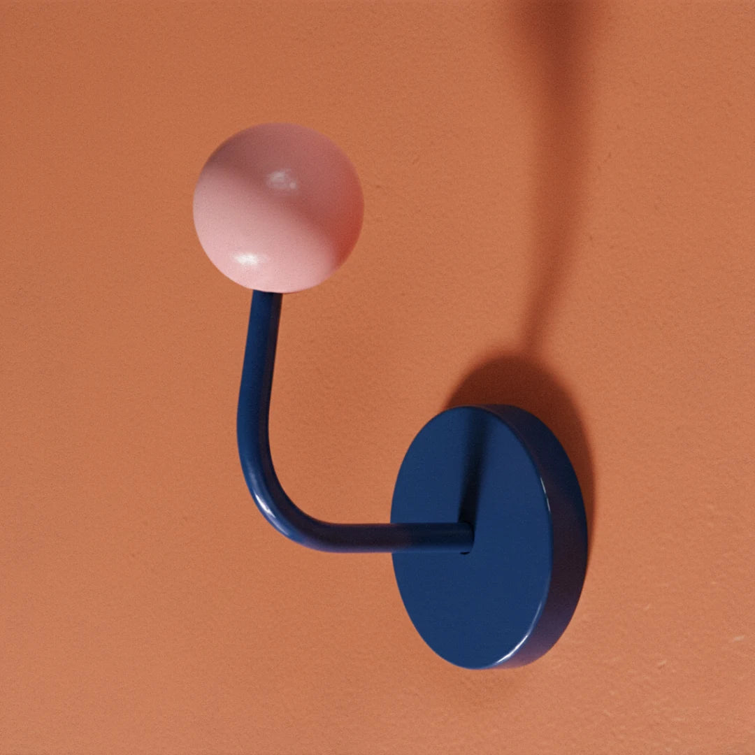 Wall hook with pink spherical top and blue circular base on an orange background