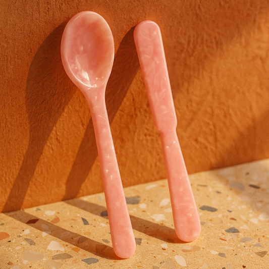 Two pink spoons on a textured surface with an orange-brown background