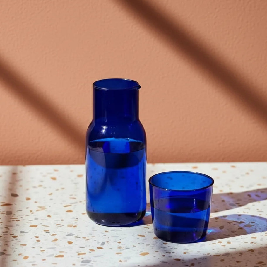 Blue glass carafe and cup on a textured surface with a brown background