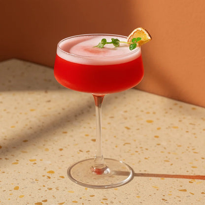 Red cocktail with a white foam top and a slice of lemon on a terrazzo countertop.
