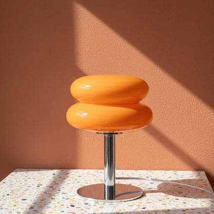 Orange stool with a metallic base on a terrazzo surface against a peach wall.