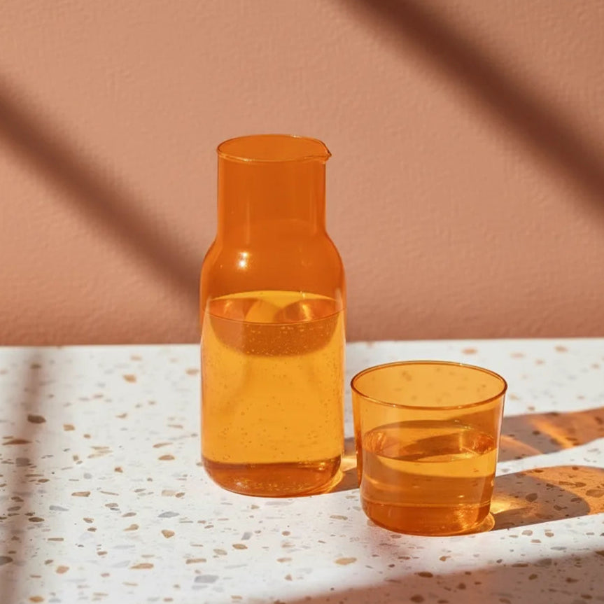 Orange carafe and glass with water on a textured surface with a brown background