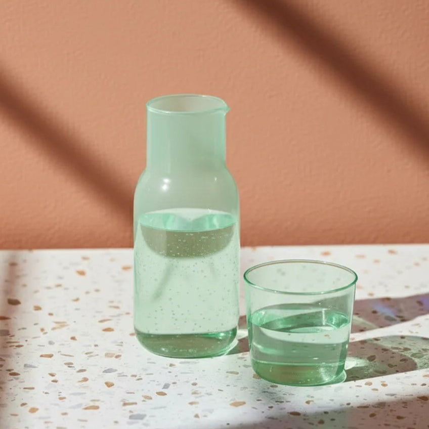 Green glass carafe and cup on a speckled surface with a brown background