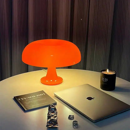 Orange lamp, laptop, book, and candle on a table with dark curtains in the background